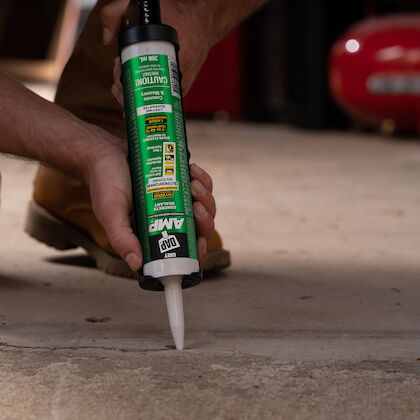 Hand applying DAP AMP sealant into a crack in a concrete floor