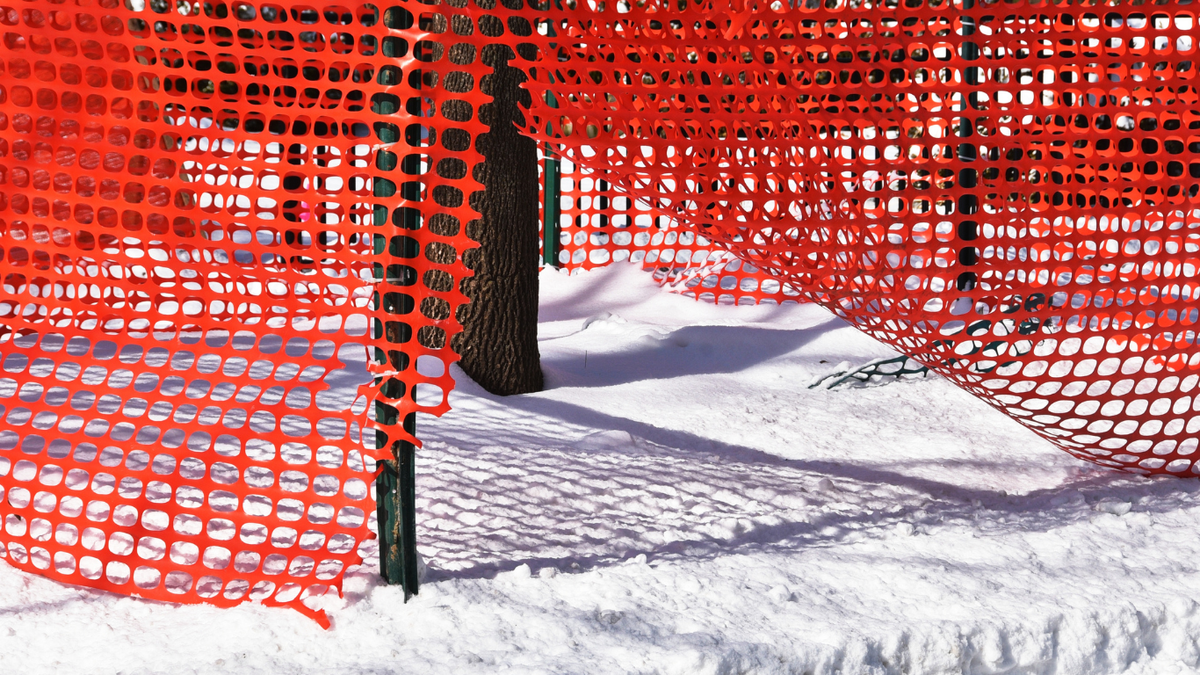 Orange plastic snow and construction fencing set up around trees in the snow