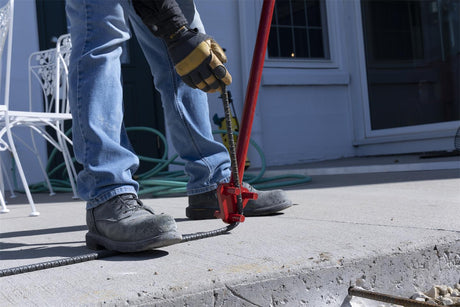 Worker bending rebar with a red manual rebar bender on a concrete slab