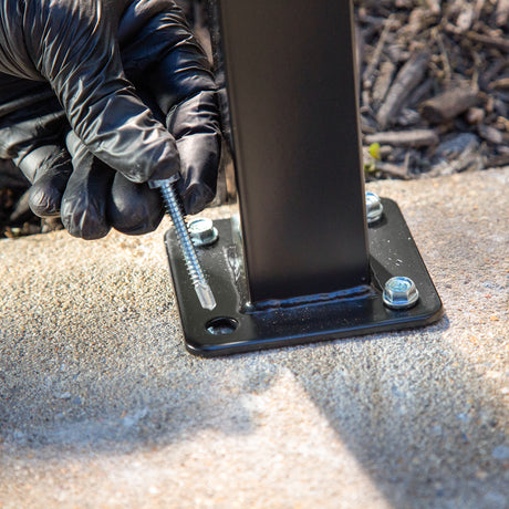 Mains gantées fixant la plaque d'un poteau noir sur le béton avec une vis