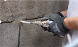 Grout injection with a gun into a stone wall joint, gloved hands