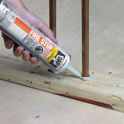 Hand applying DAP Fire Stop sealant around copper pipes in wood